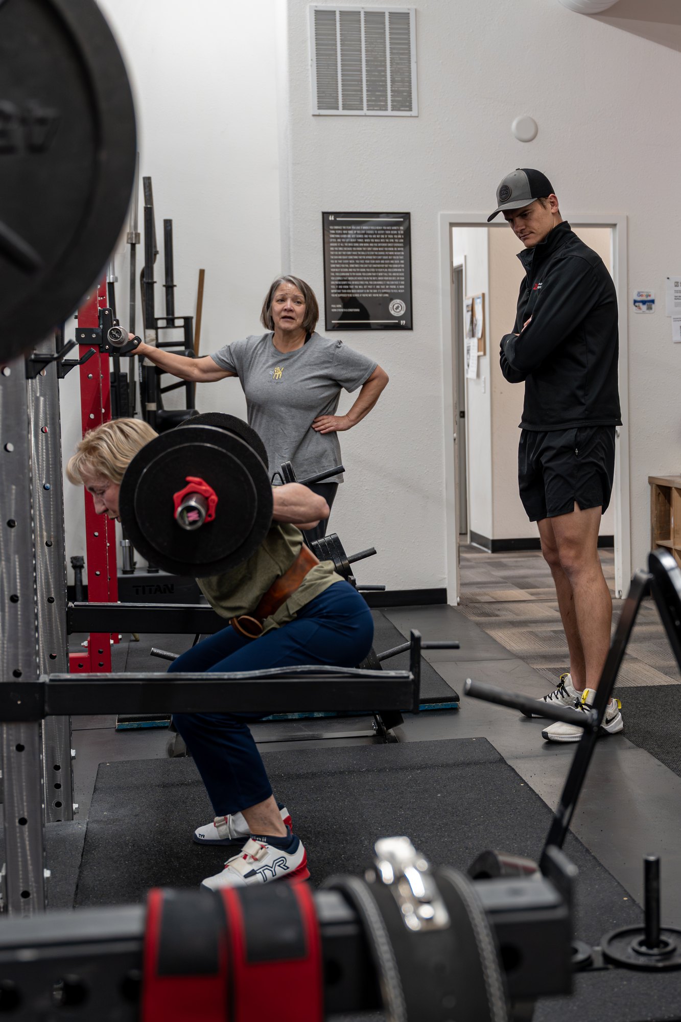 A coach and spotter supporting an adult through a barbell squat
